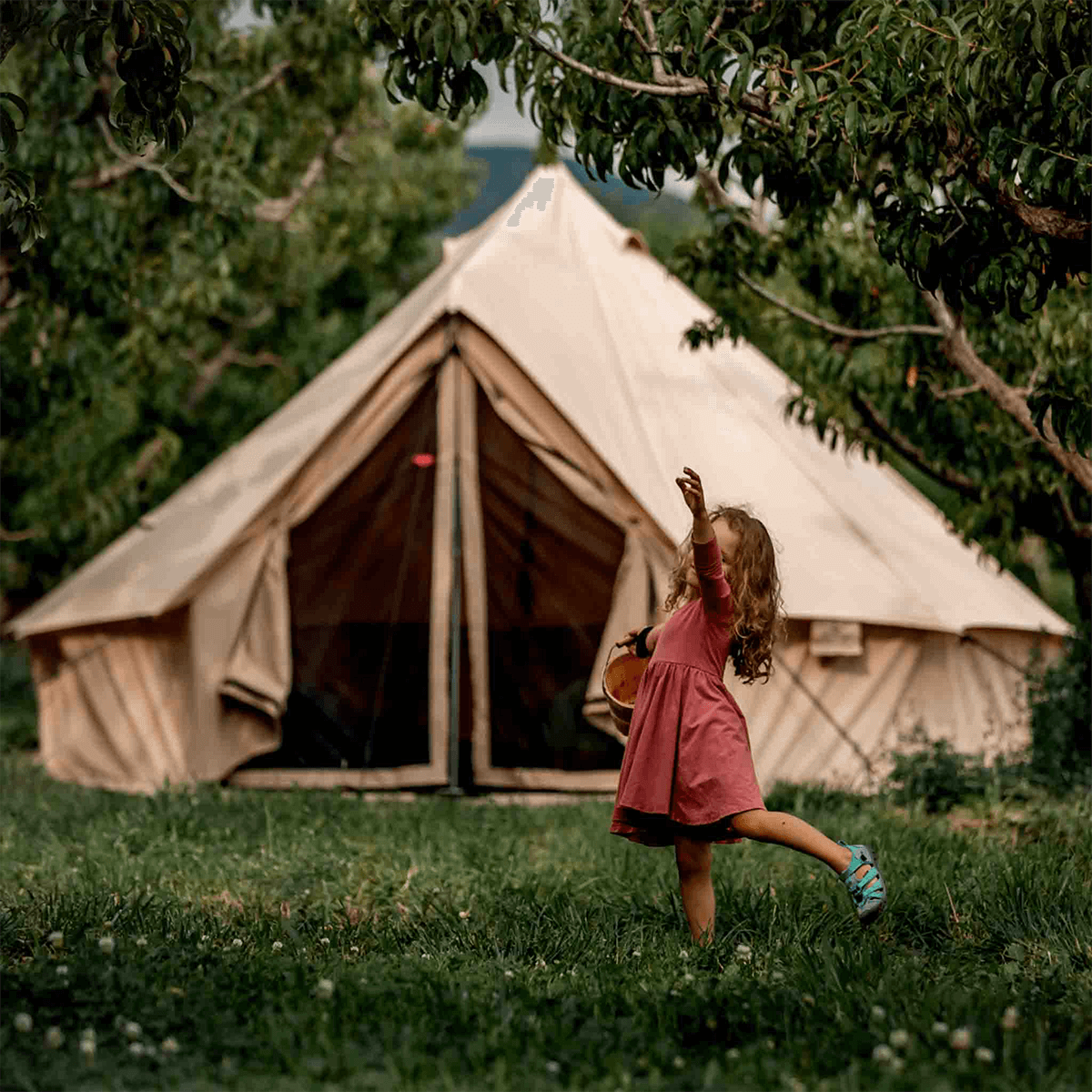 Sandstone beige 16-foot Regatta Bell Tent by White Duck Outdoors with a girl playing outside in natural outdoor setting.
