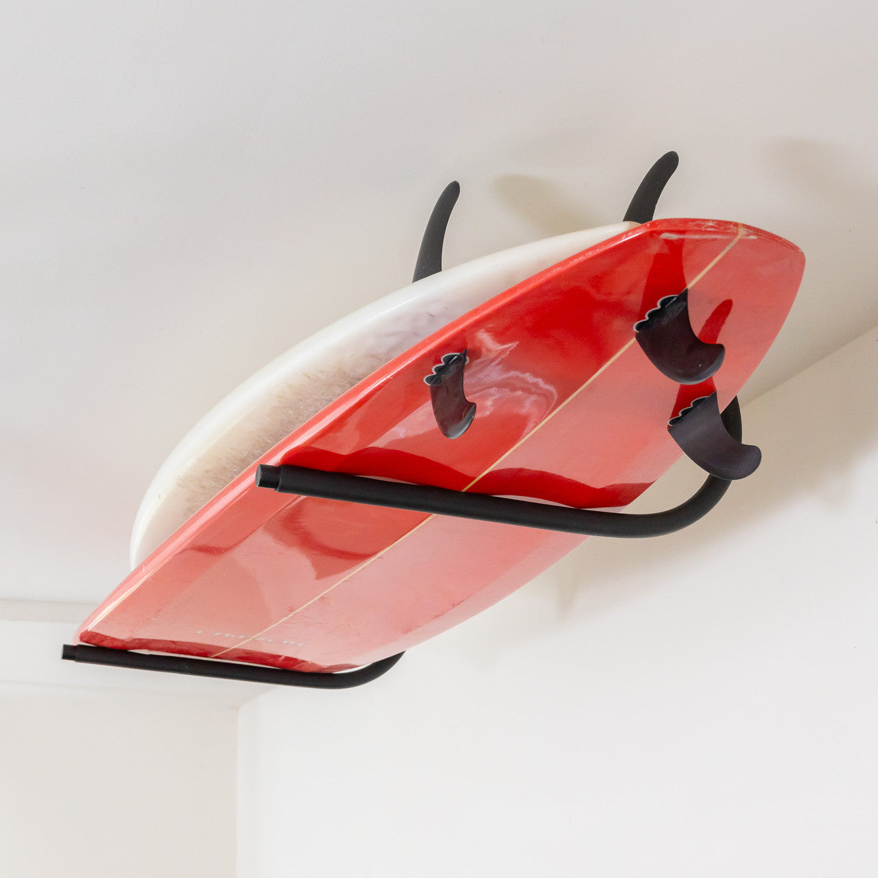 Red and white surfboard leaning against a white wall with a black rack.