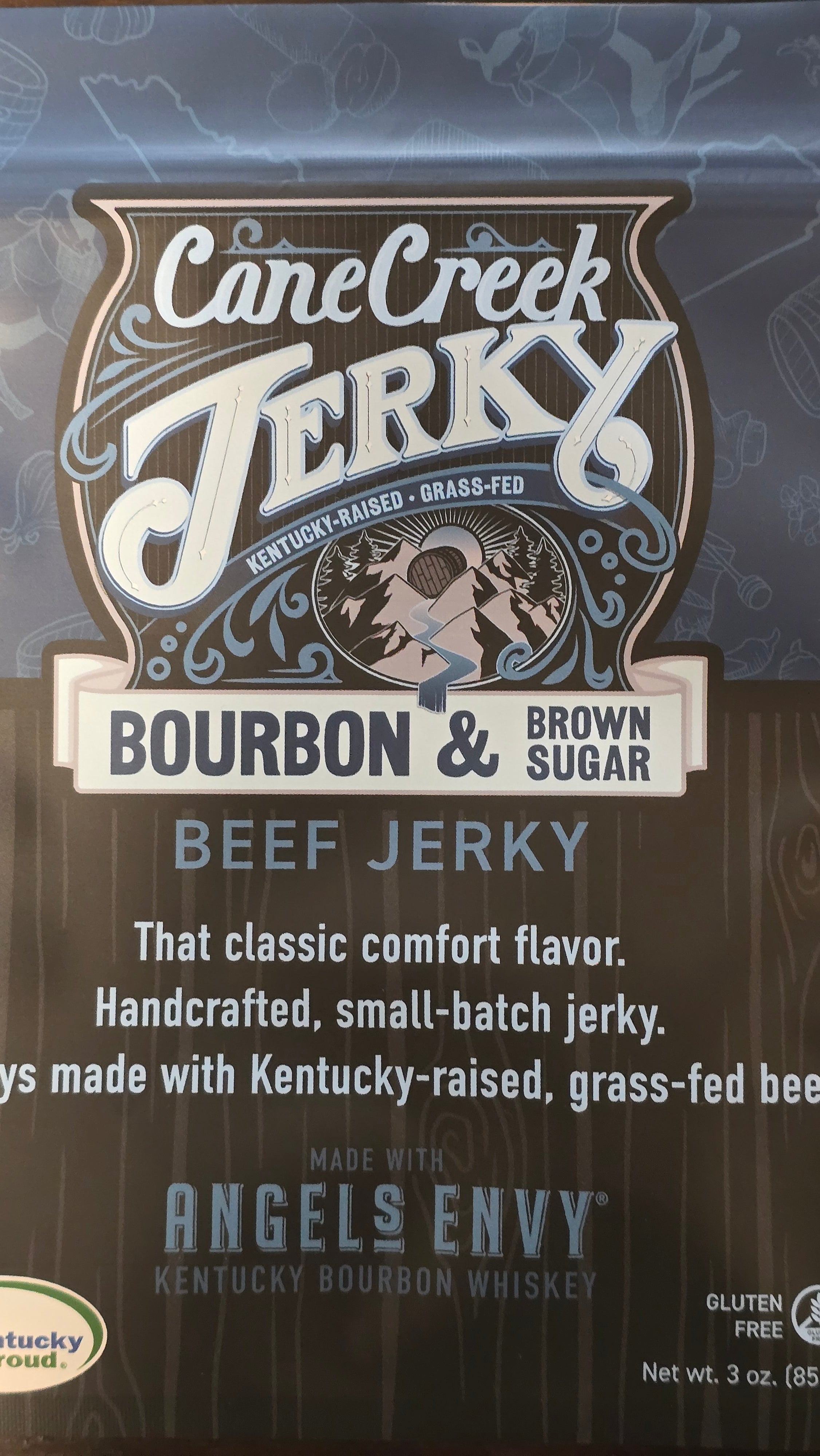 Cane Creek Jerky Bourbon & Brown Sugar Beef Jerky with glossy, seasoned beef slices on a wooden surface.