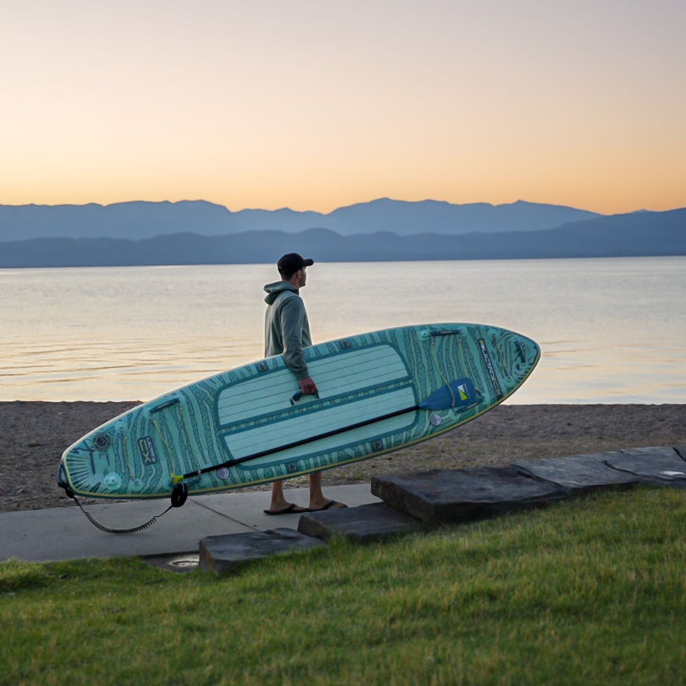 iROCKER US CX ULTRA™ 3.0 paddle board on water with paddle, showcasing durable design and sleek shape for stand-up paddling.