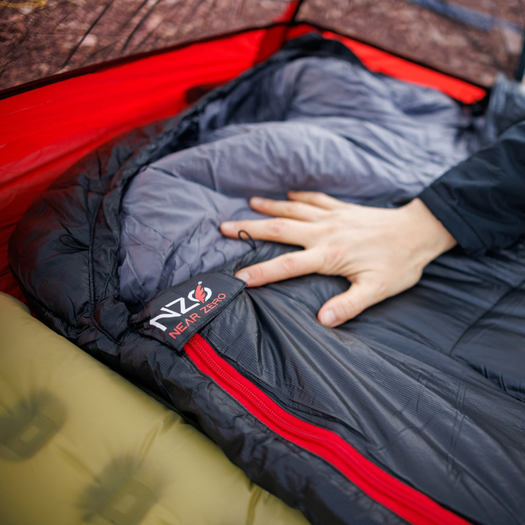 Near Zero Outdoor Gear Peralta 25 synthetic sleeping bag laid out on a campsite, showing its lightweight, insulated design for outdoor sleep.