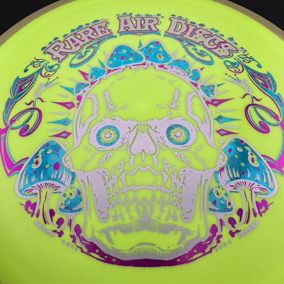 Rare Air Discs Fission Defy Crushin' Amanitas VIP 2.0 disc golf disc laid on grass with vibrant design and branding details.