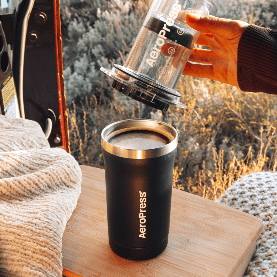 A person using an Aeropress to make coffee outdoors.