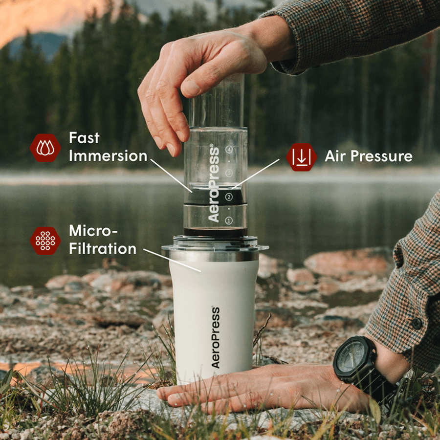Person using an Aeropress coffee maker outdoors by a lake