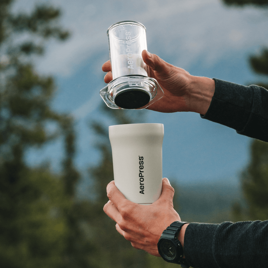 Person holding an Aeropress coffee maker with a blurred natural background