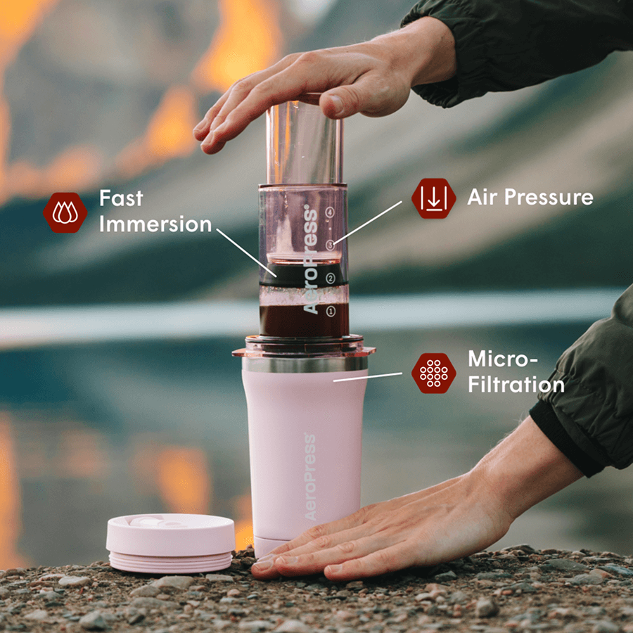 Aeropress coffee maker being used with a hand holding it over a natural background