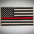 American flag made from recycled fire hose with a thin red line, symbolizing firefighting pride, on a white background.