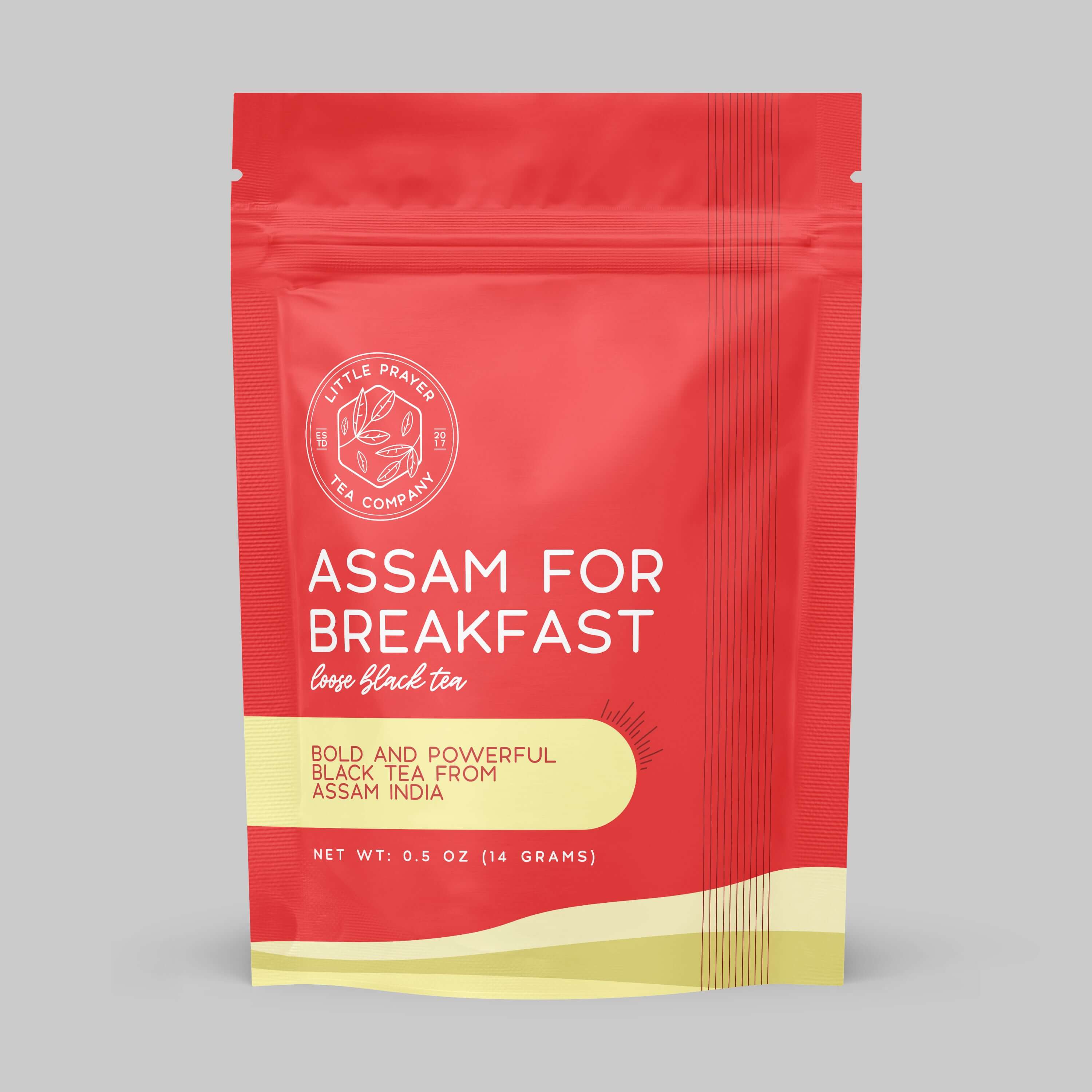 Assam tea from Little Prayer Tea Company displayed in a white cup with loose tea leaves on a wooden table.
