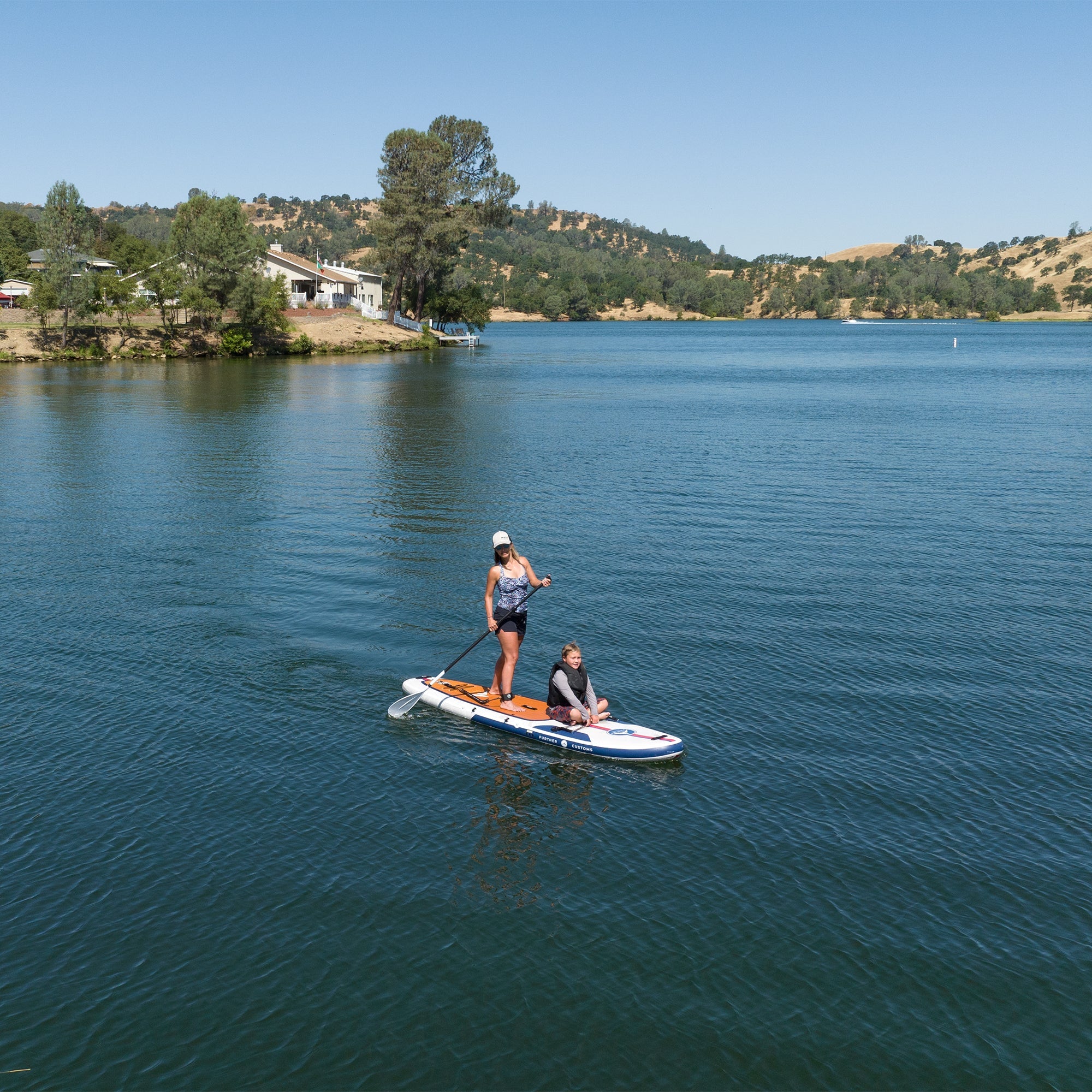 Two riders on a 11-foot Avalon Mariner paddleboard by Further Customs, shown on calm water with paddles in hand.