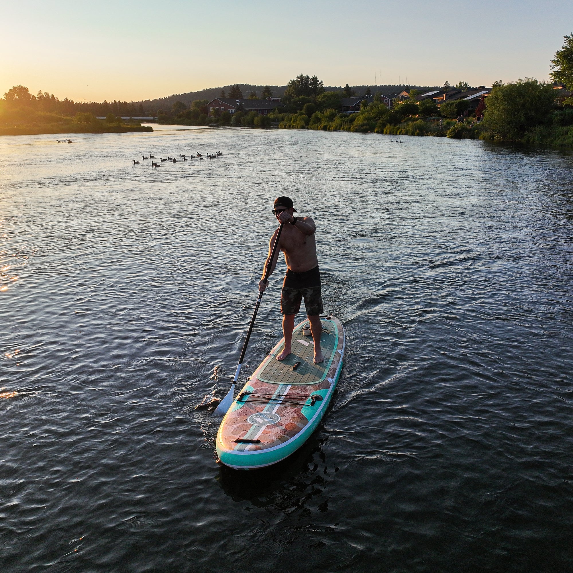 11'0 Tamarack Sage paddleboard by Further Customs, shown on the river with a person standing and paddling on the water.