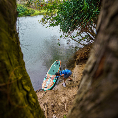 Inflatable 11-foot Tamarack Sage paddleboard by Further Customs, shown on water with lush trees in the background.