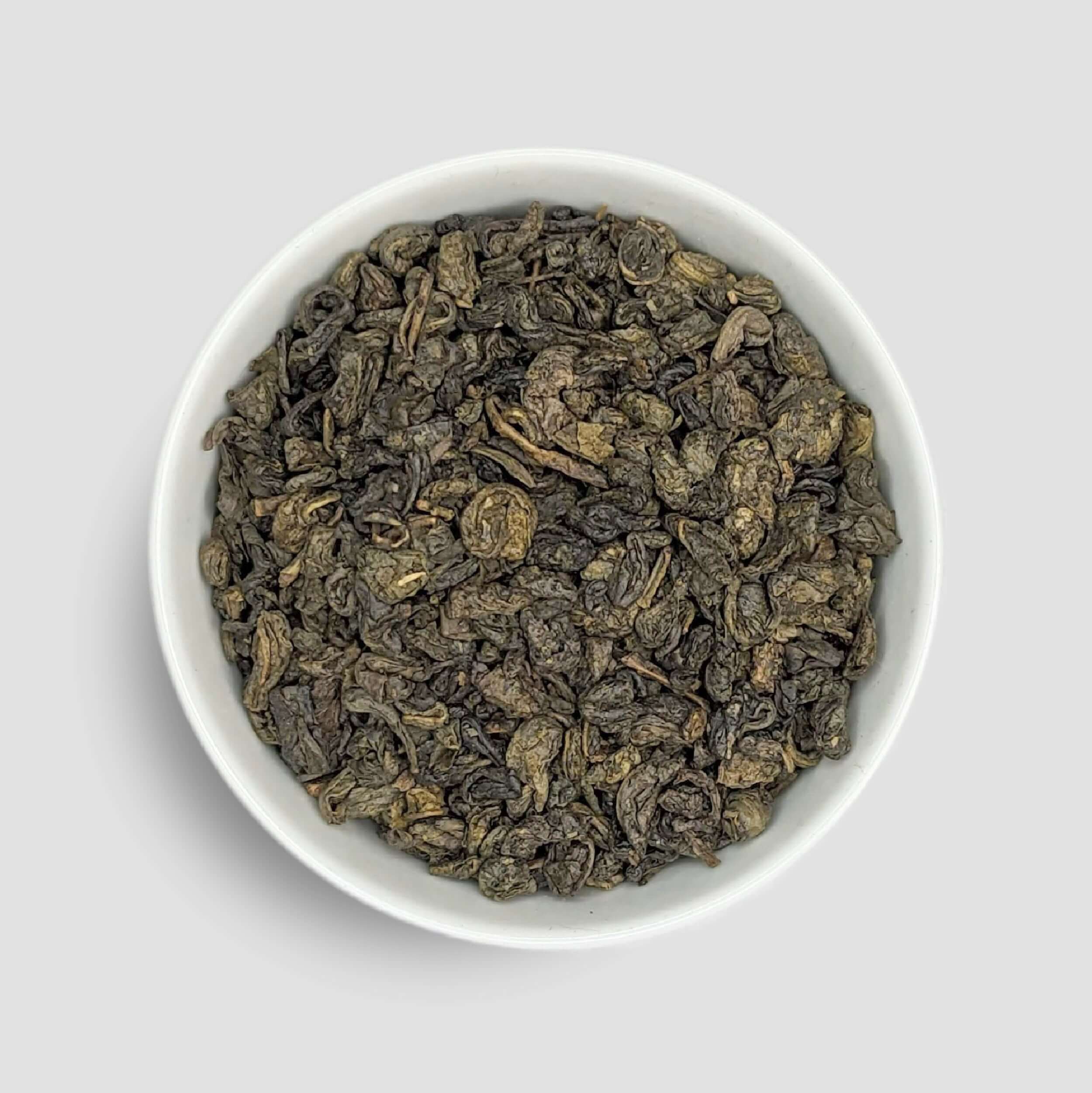 Fresh gunpowder green tea leaves in a bowl, showcasing tightly rolled green tea pellets from Little Prayer Tea Company.