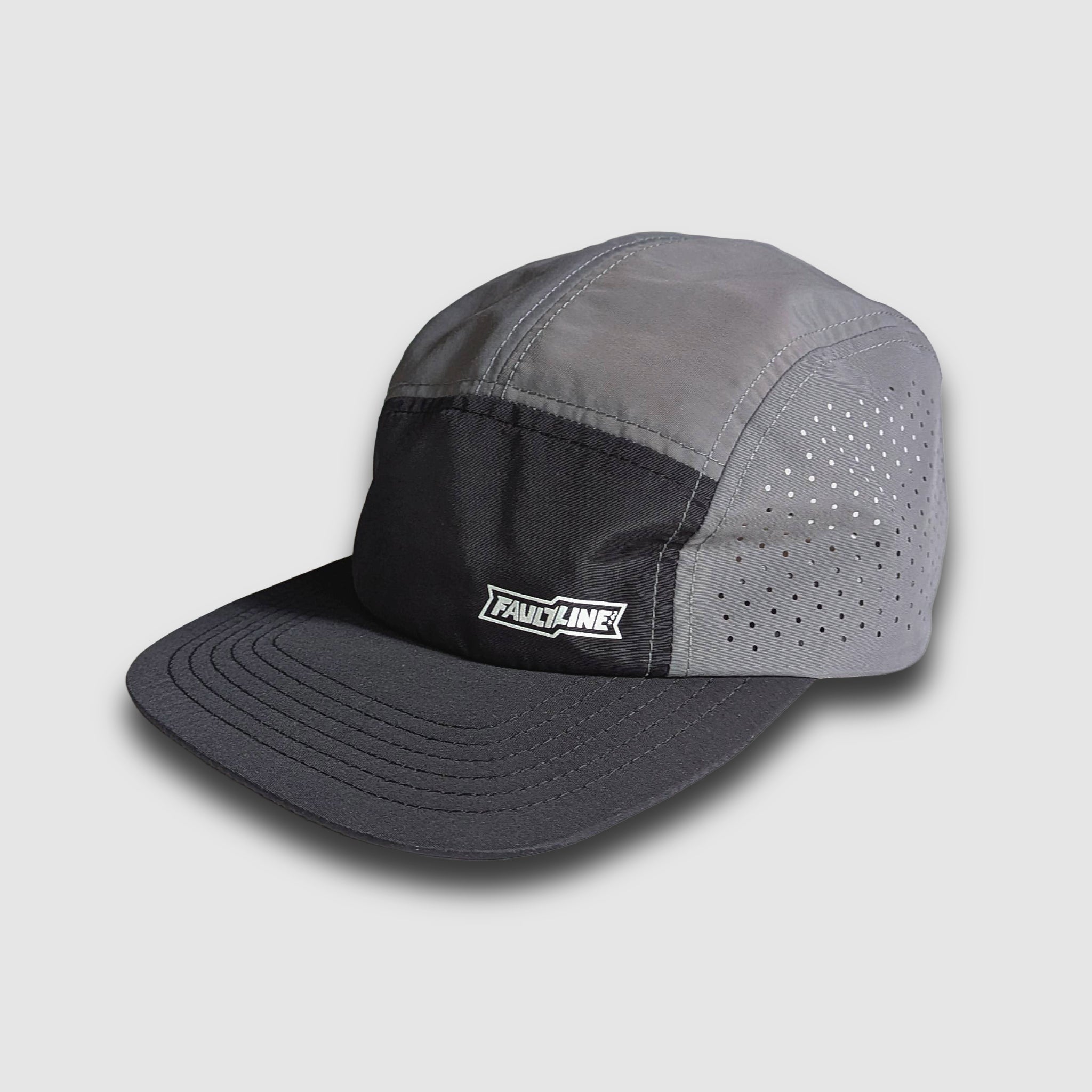 Black and grey crushable 5-panel camper hat by Faultline395, shown in a stylish outdoor setting.