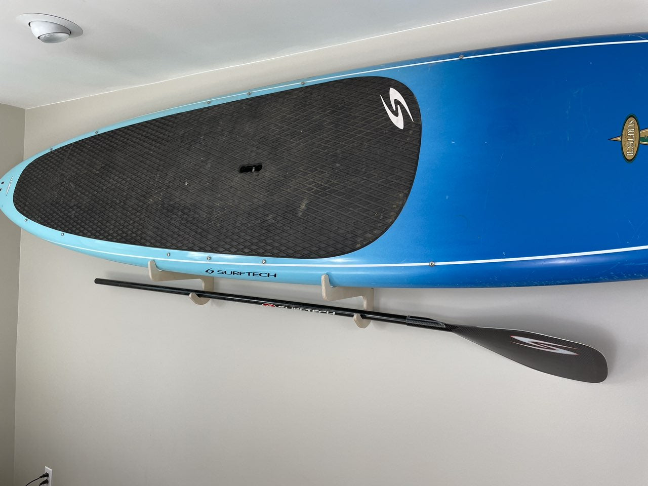 Rado Racks THE PORT SUP paddle board rack mounted on wall, holding a paddle board and paddle for easy storage and organization.