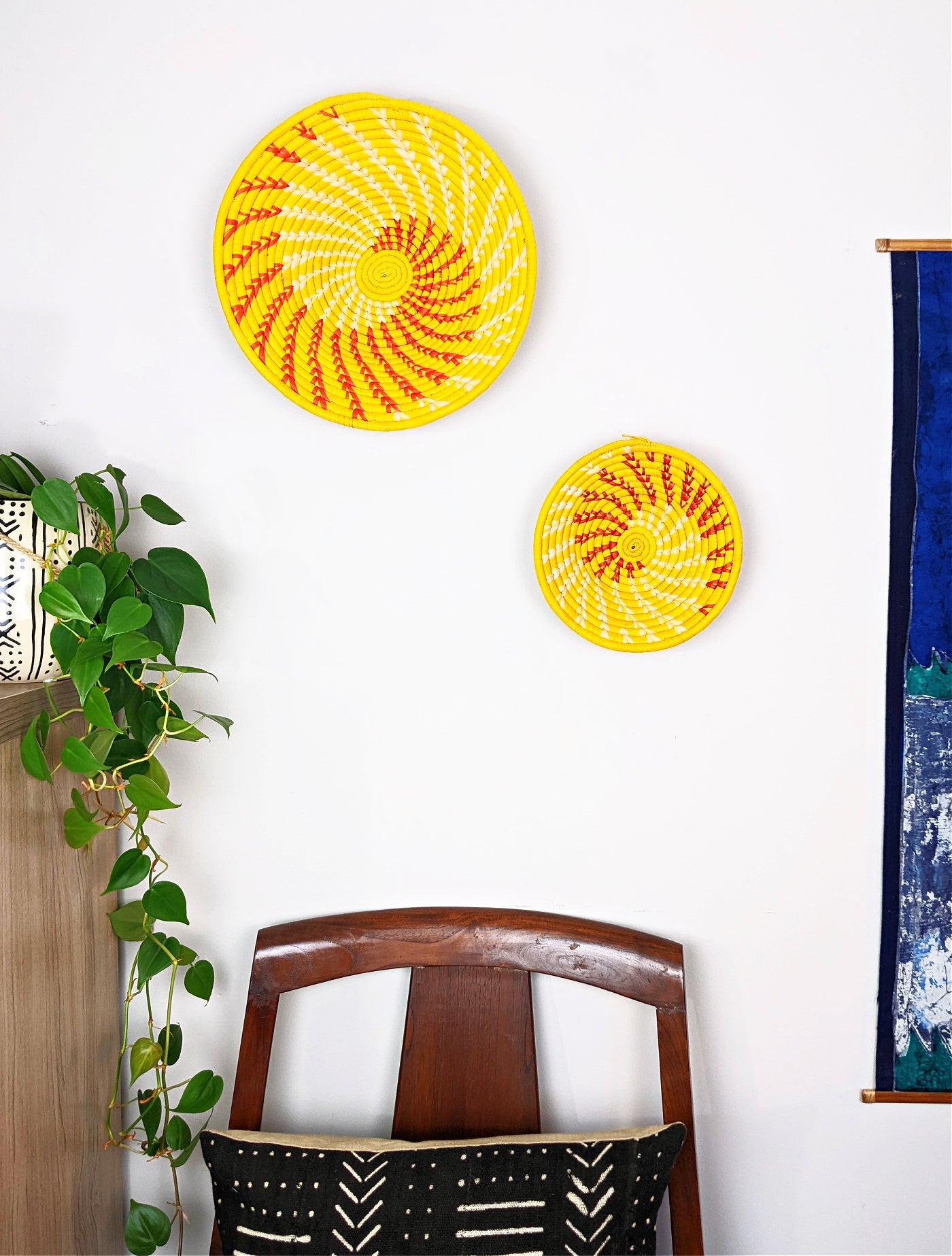 Large yellow woven African basket from Reflektion Design hanging on a wall, showcasing its textured woven pattern and vibrant color.