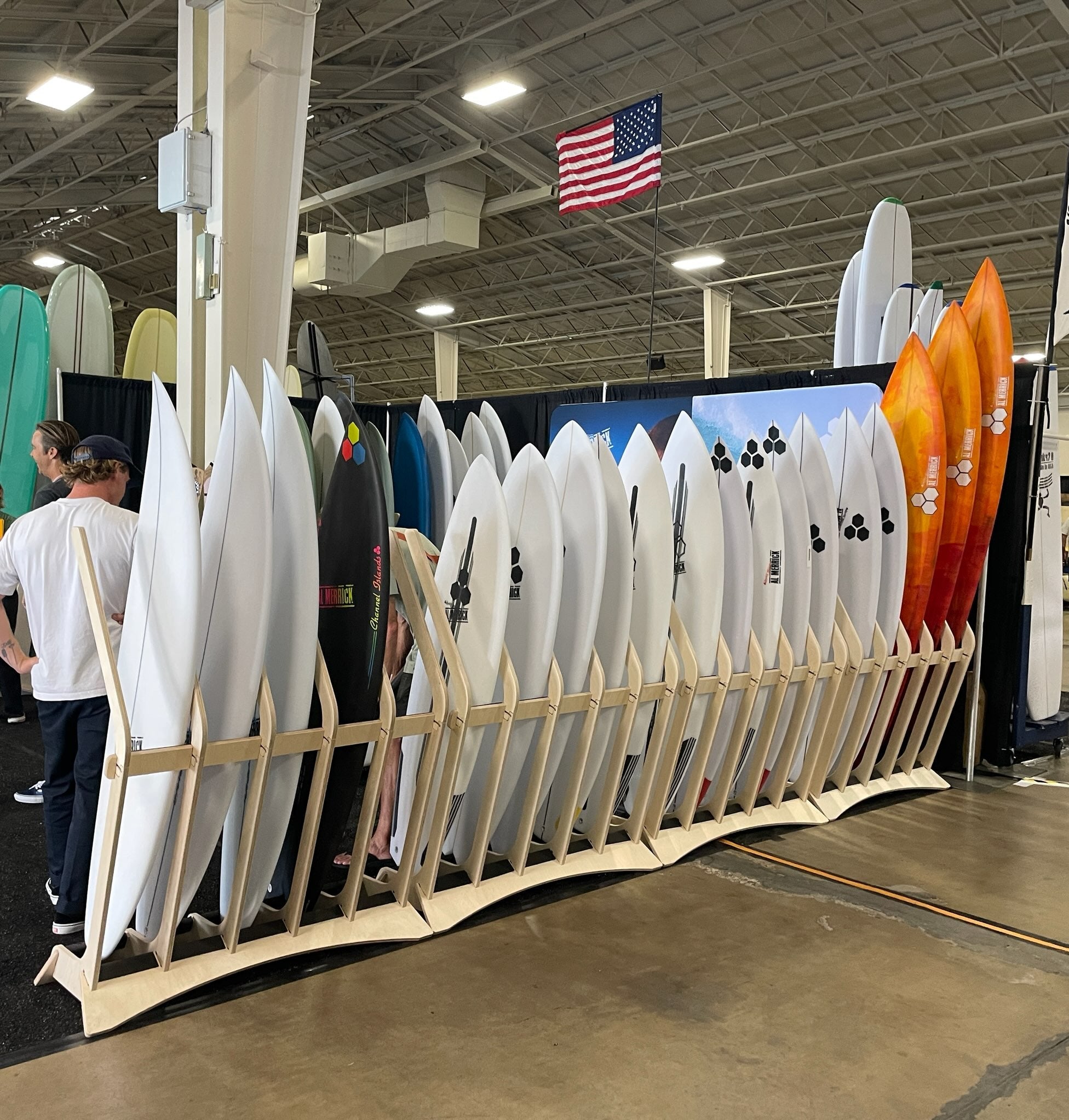 Display of surfboards and paddles at a trade show with people in the background.