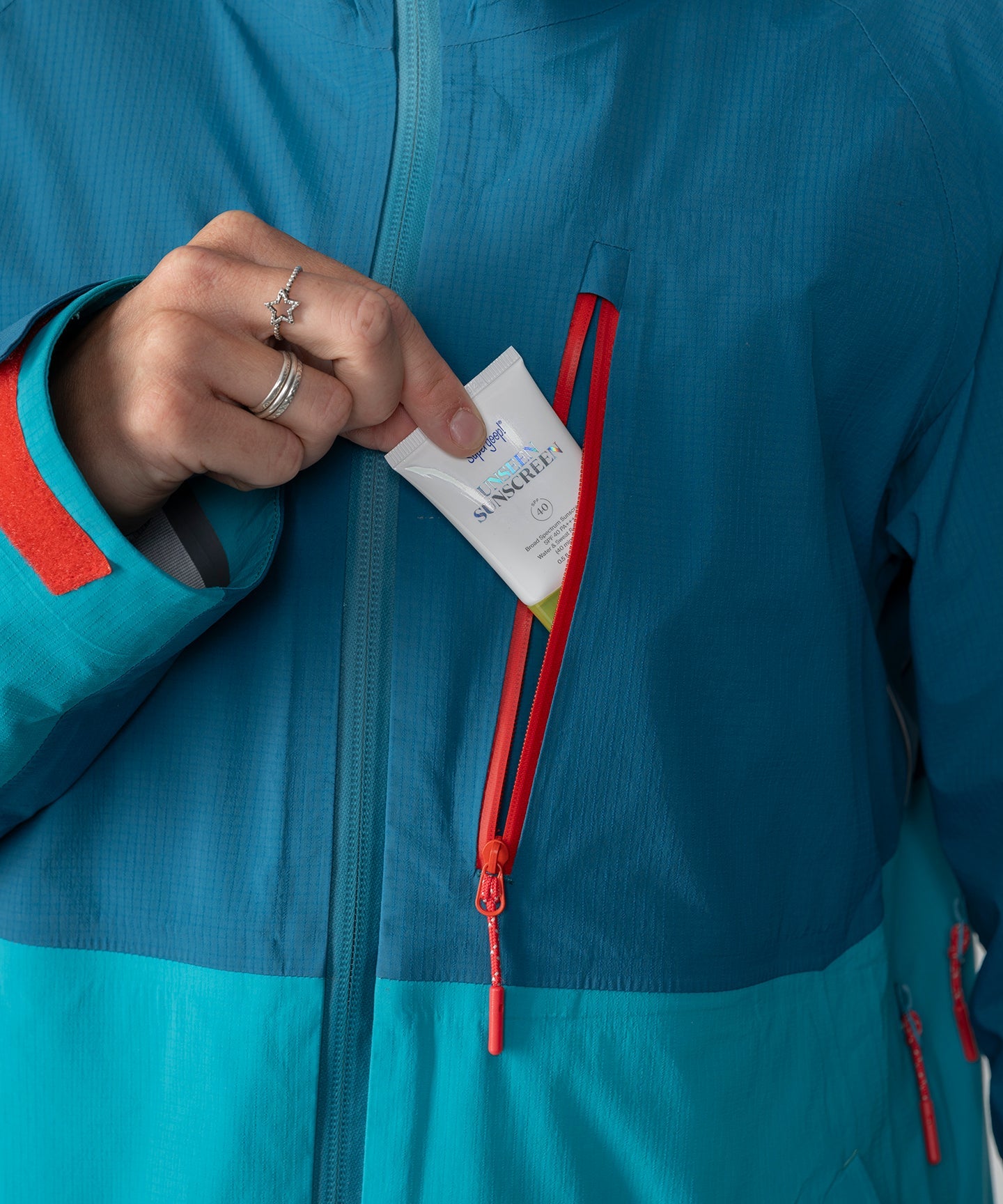 Dark teal Strafe Outerwear Meadow 3L shell jacket displayed on a hanger with a scenic outdoor backdrop.