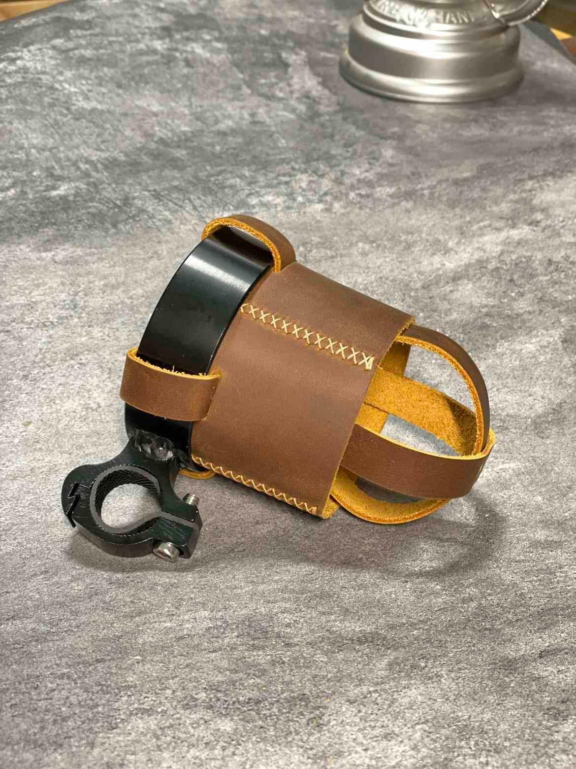 Handmade leather motorcycle water bottle holder mounted on bike, with adjustable strap, by Bean's Moto Booth motorcycle accessories.