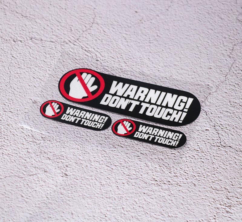 Decorative 3-inch "WARNING DON’T TOUCH" sticker by Bean's Moto Booth, featuring bold warning text on a clear background.