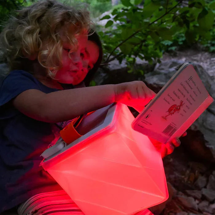 Children reading with the Alpenglow Readiness Supply PackLite Titan 2-in-1 Power Lantern glowing red in an outdoor setting.