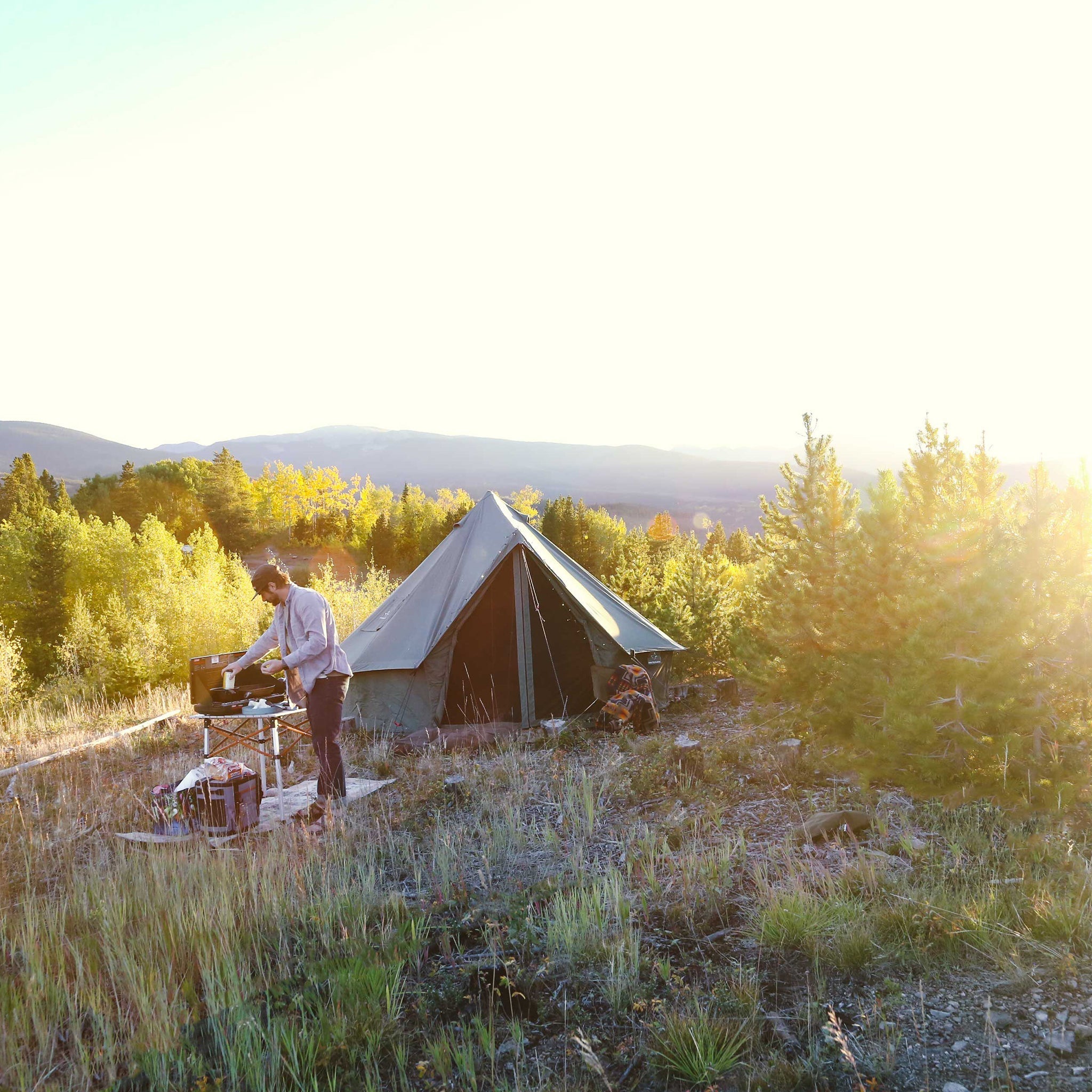 White Duck Outdoors Regatta Bell Tent in Boulder Grey set in a forest with a man cooking outside.