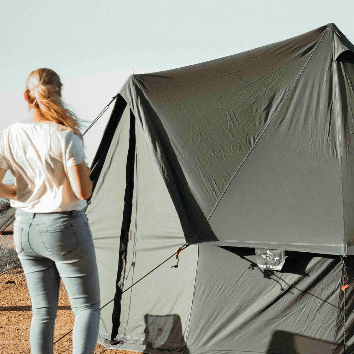 White Duck Outdoors 20-foot Regatta Bell Tent in Boulder Grey with a woman standing in front of the tent.
