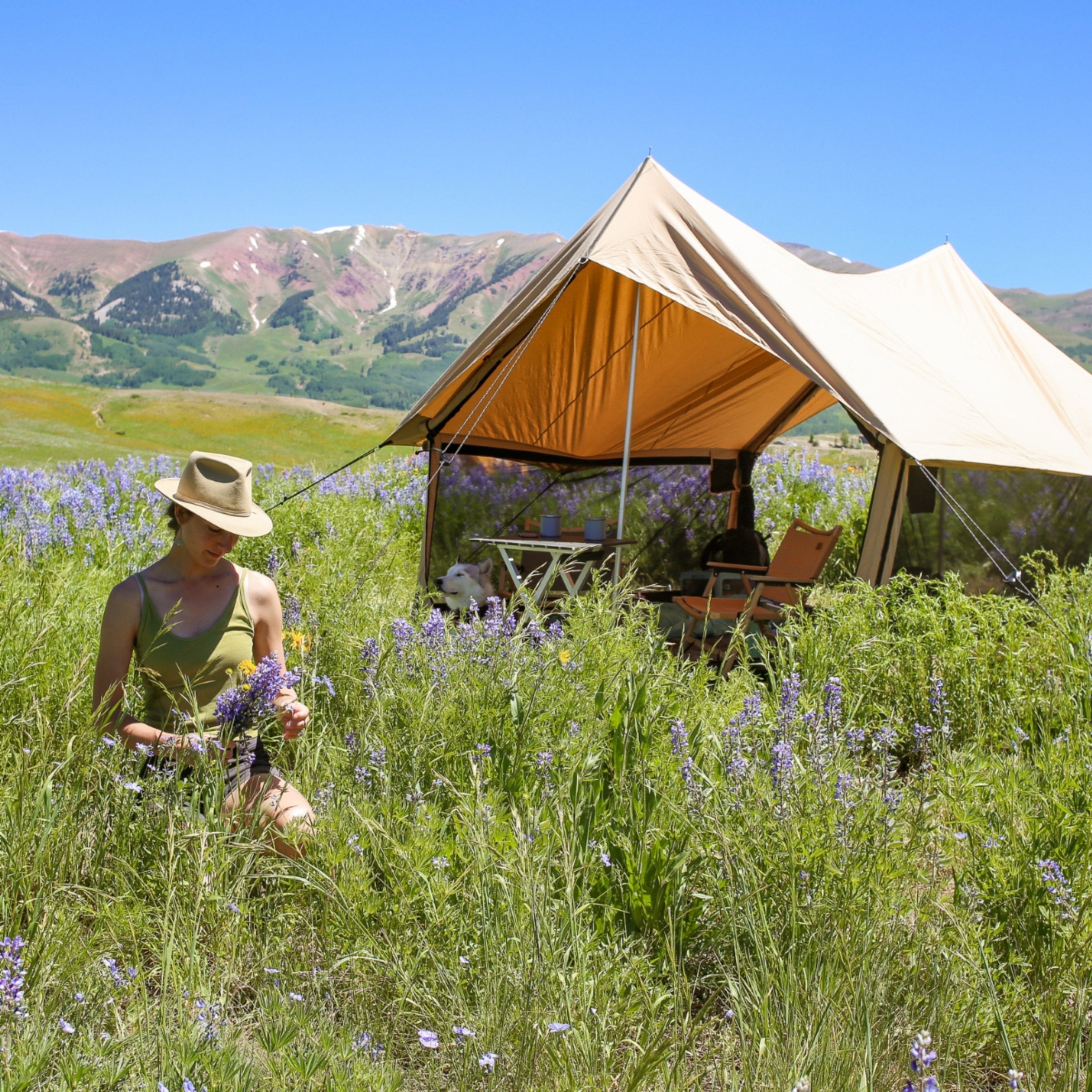 White Duck Outdoors Rover Scout Tent set up in a grassy area with flowers, shown outdoors with a woman nearby.
