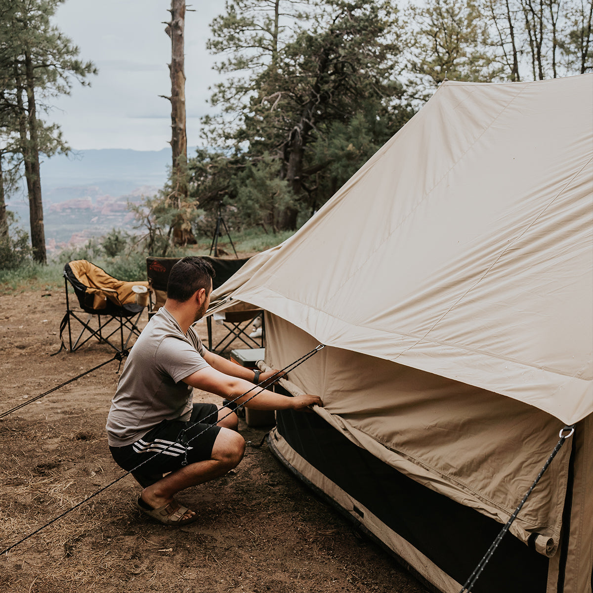 White Duck Outdoors Rover Scout Tent set up in a forest, with a person rolling up the tent walls.