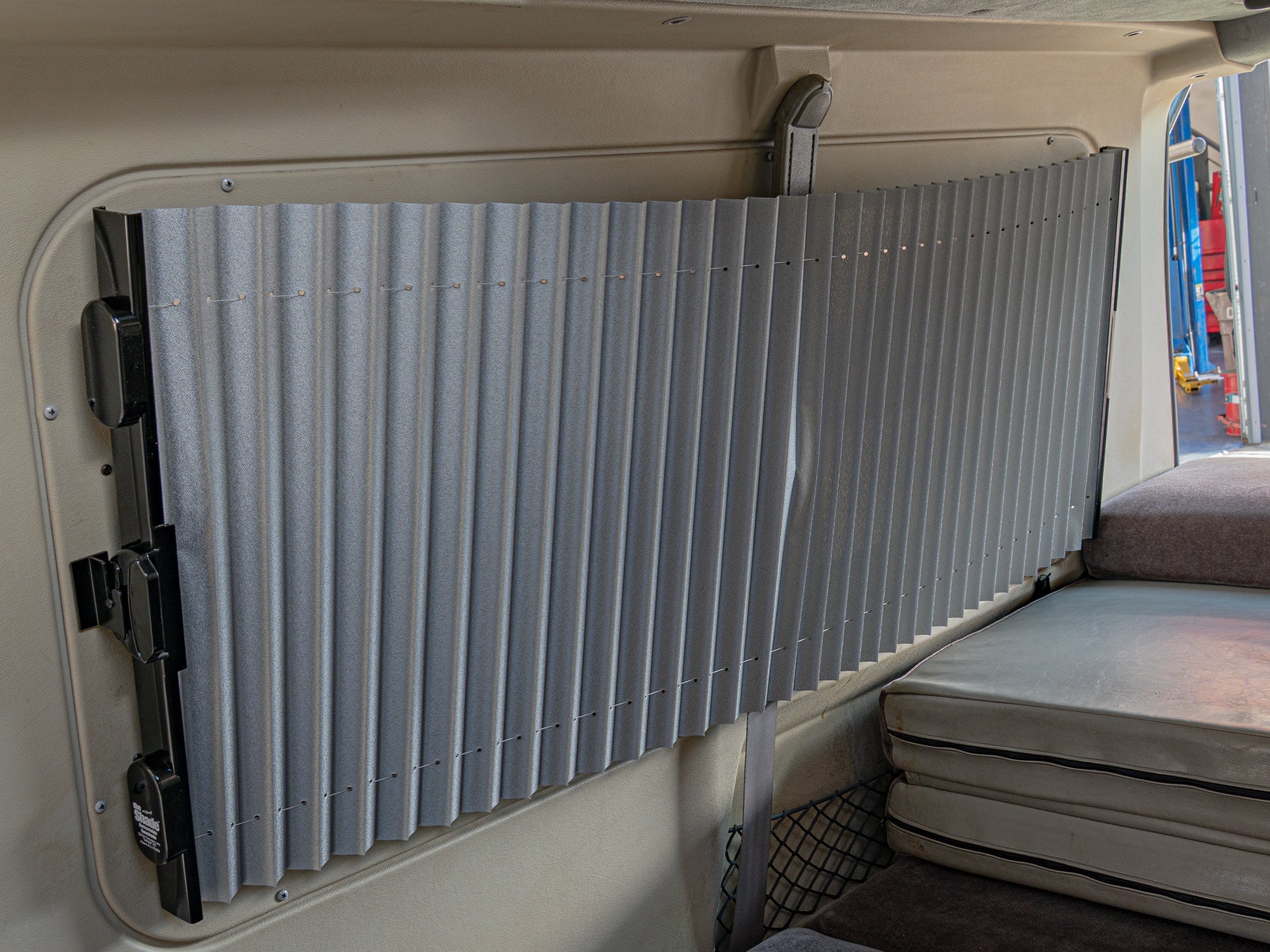 GoWesty retracting sun and privacy shade installed in the right rear of a Bus/Vanagon/Eurovan, partially open for sunlight and privacy.