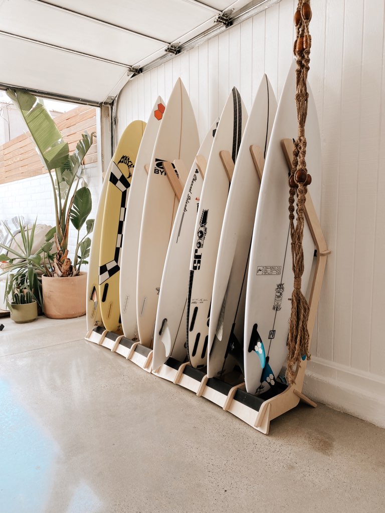 Row of surfboards on a stand against a white wall with plants and a pool in the background.