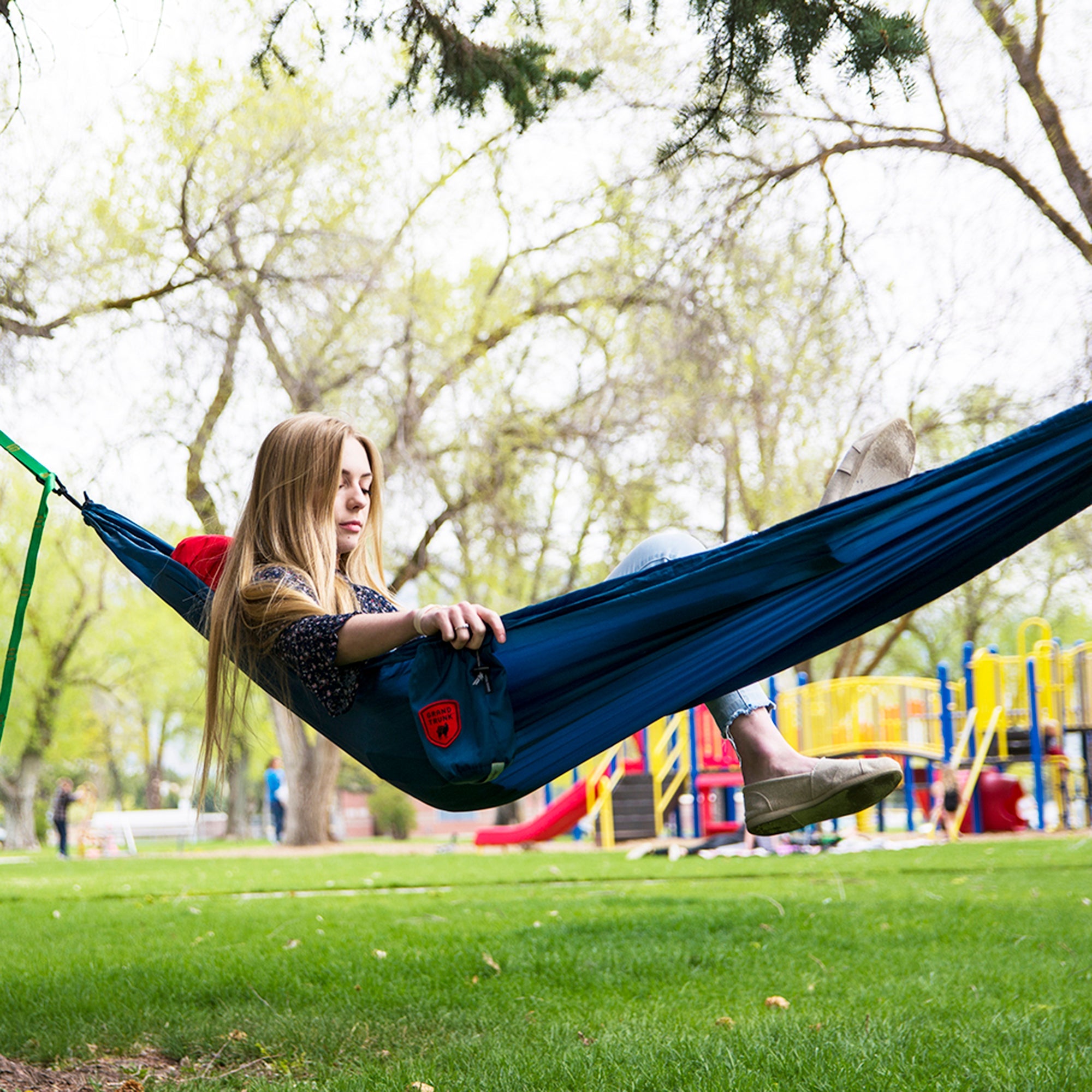 Ultralight GrandTrunk starter hammock set up between two trees in a lush green outdoor setting.