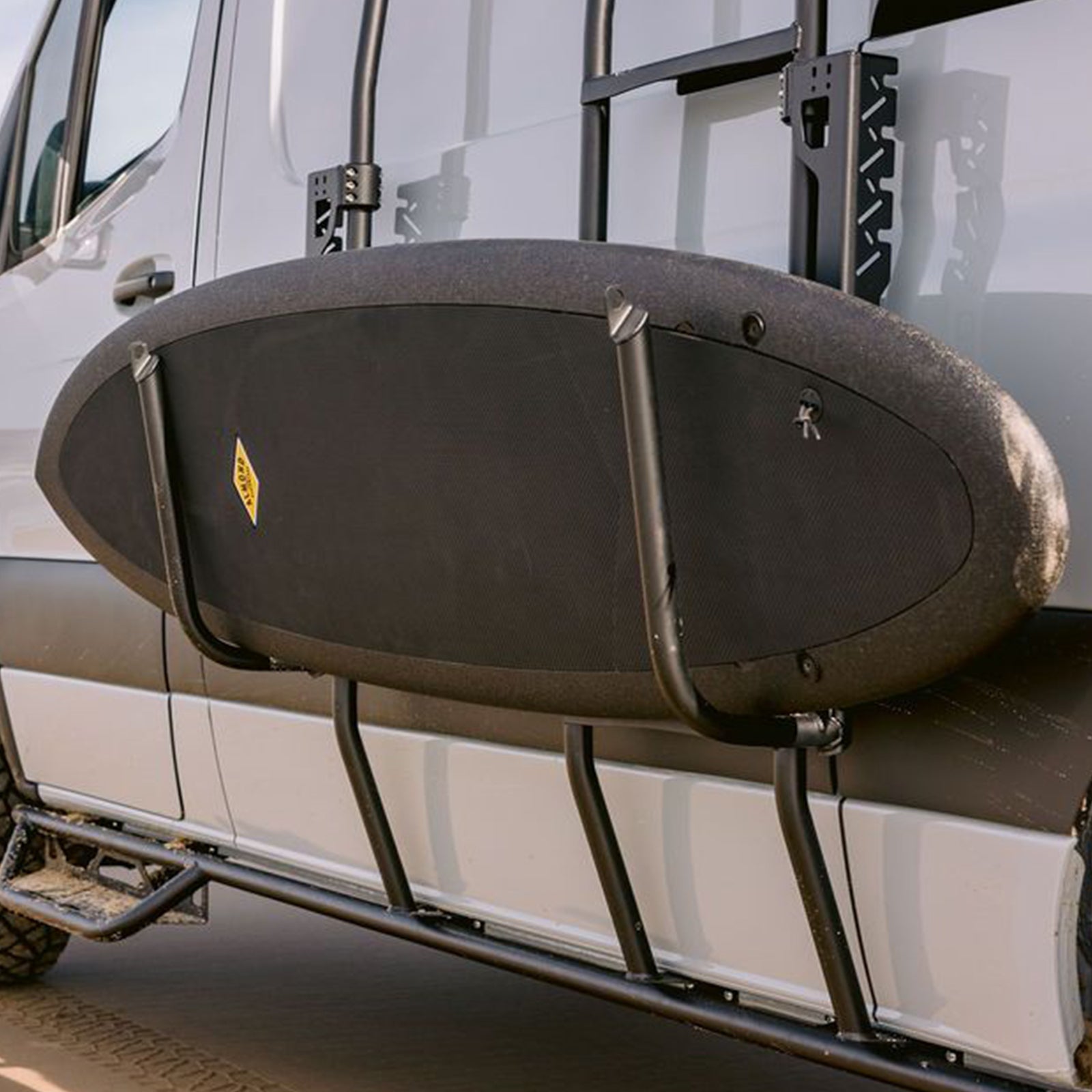 Sprinter Exterior Surf Rack Set by The Van Mart mounted on a van, holding surfboards against a scenic backdrop.