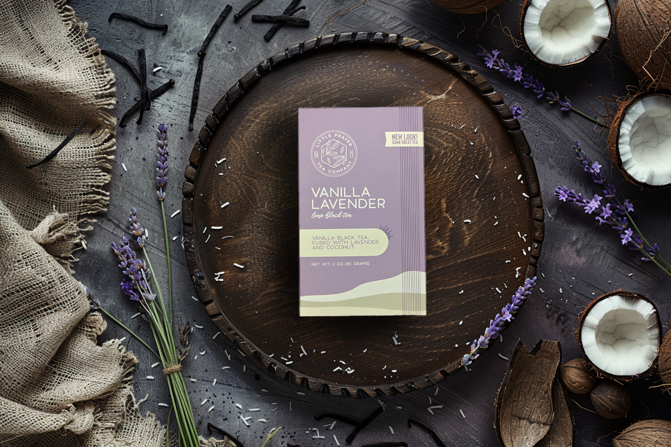 A cup of vanilla lavender black tea from Little Prayer Tea Company with tea leaves and vanilla bean on a wooden table.