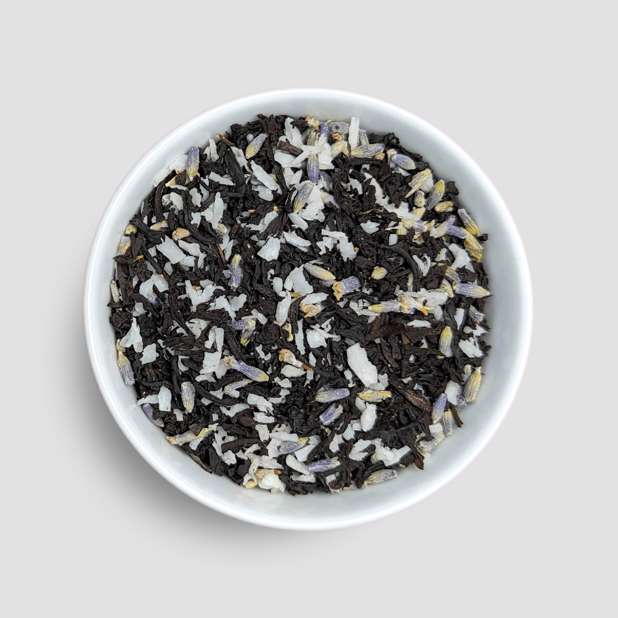 Vanilla lavender black tea from Little Prayer Tea Company displayed in a bowl with tea leaves and dried vanilla and lavender flowers.