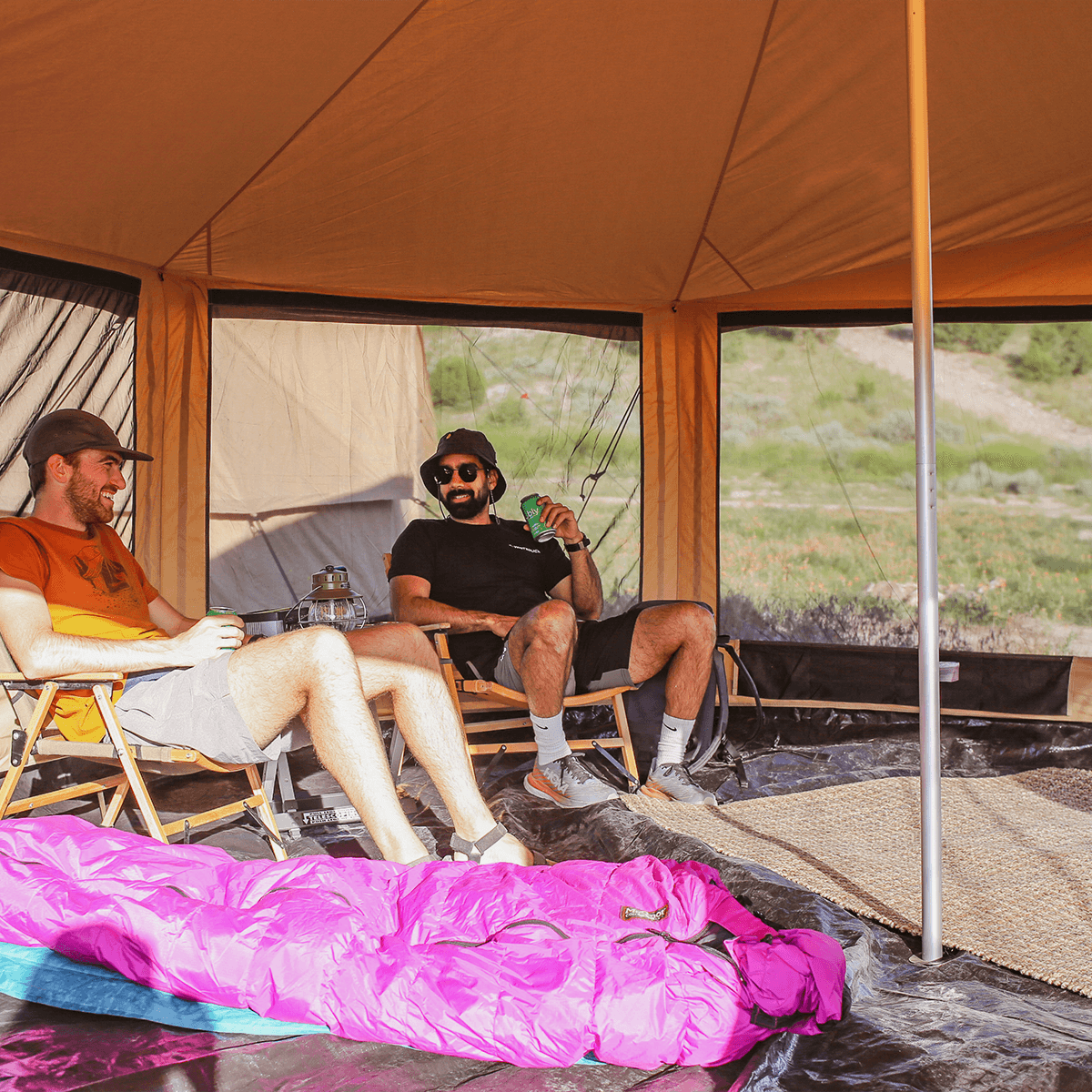 White Duck Outdoors Altimus Bell Tent set up outdoors with mesh sides, two men sitting inside enjoying the outdoor camping experience.