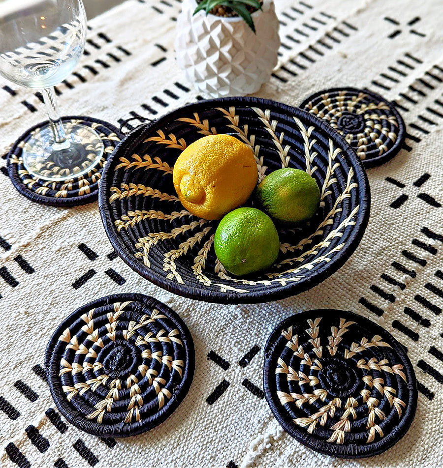 Handmade woven drink coasters set of 4 by Reflektion Design on a white tablecloth with black basket pattern, multi-colored African decor.