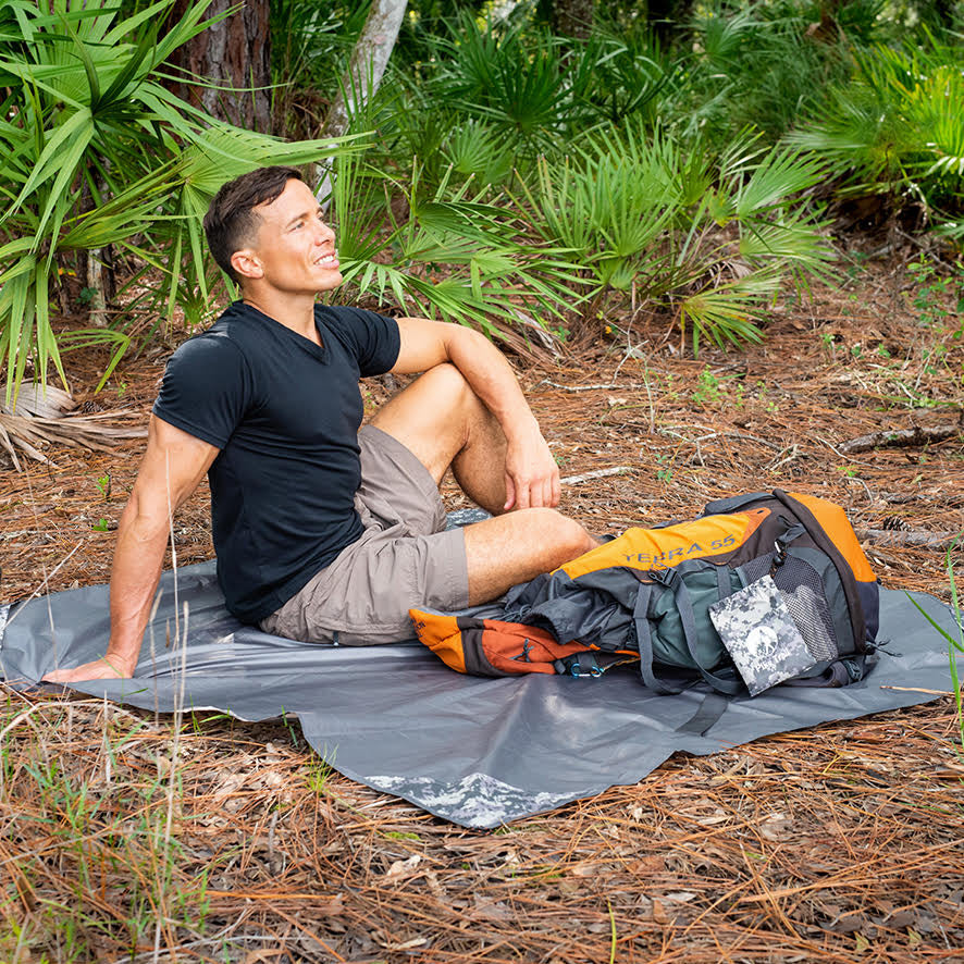 Pike Trail pocket blanket spread on grass, compact outdoor blanket for picnics and camping, in a natural outdoor setting
