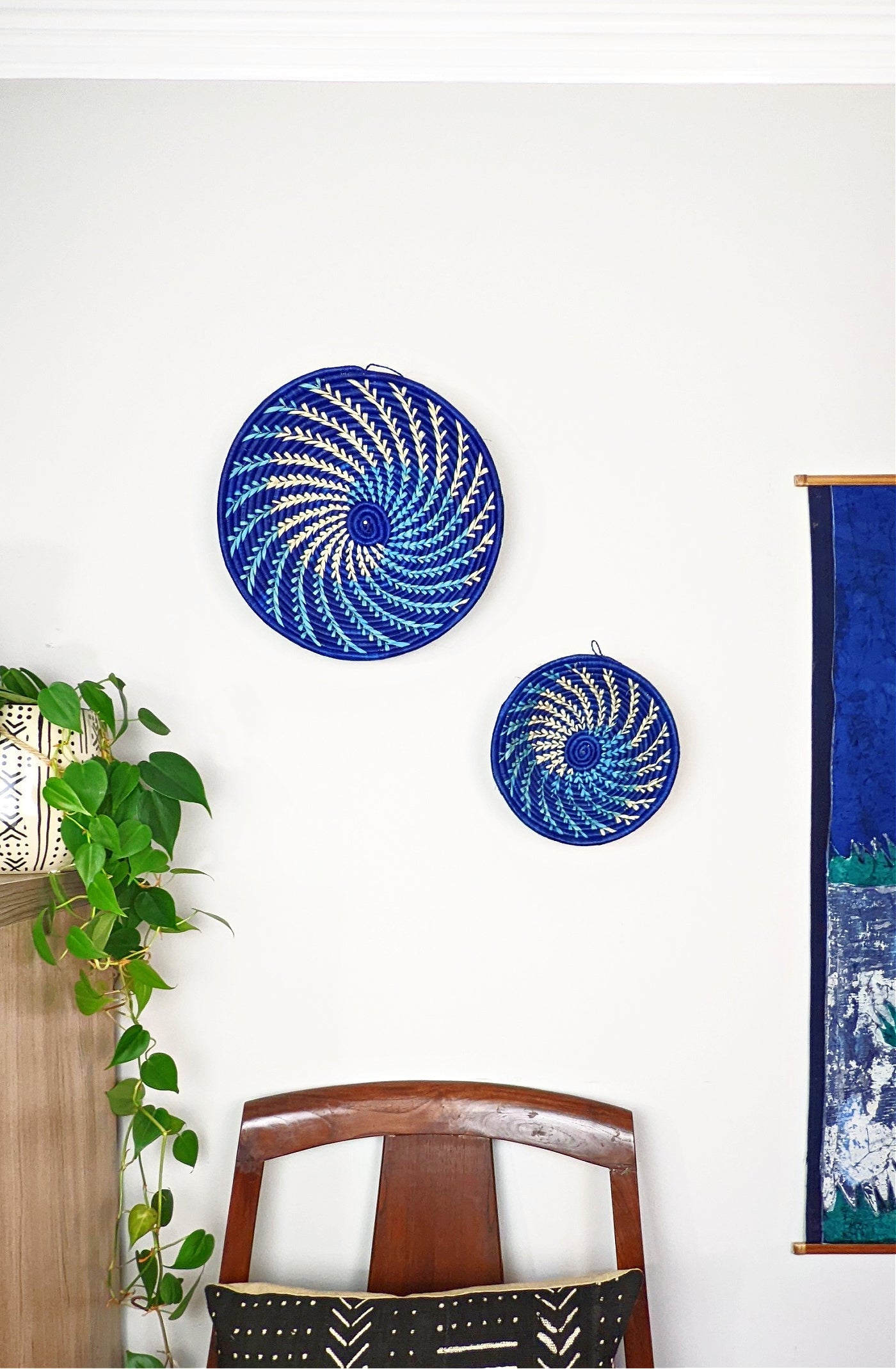 Large blue and white woven African basket by Reflektion Design hanging on a wall, showcasing intricate craftsmanship and vibrant colors.