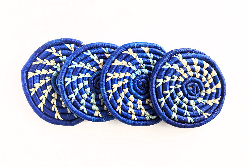 Set of four handmade woven drink coasters in blue and natural raffia by Reflektion Design, showing textured, colorful woven pattern.