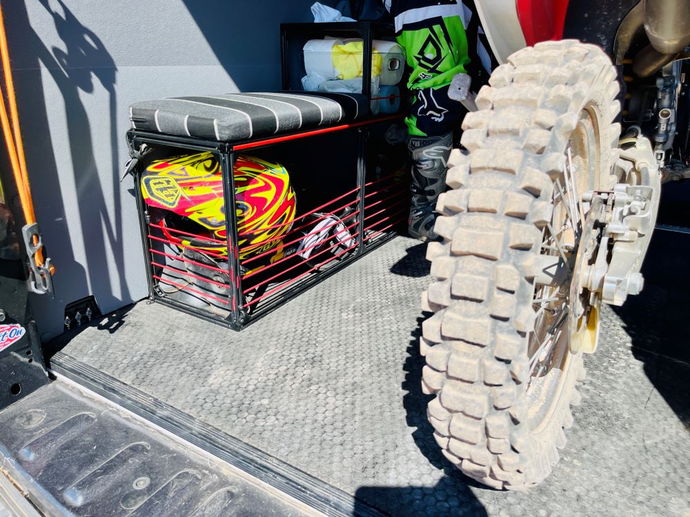 Camper van wheel well bench storage by TNTvans showing a custom-built wooden storage bench fitting over the van's wheel well.