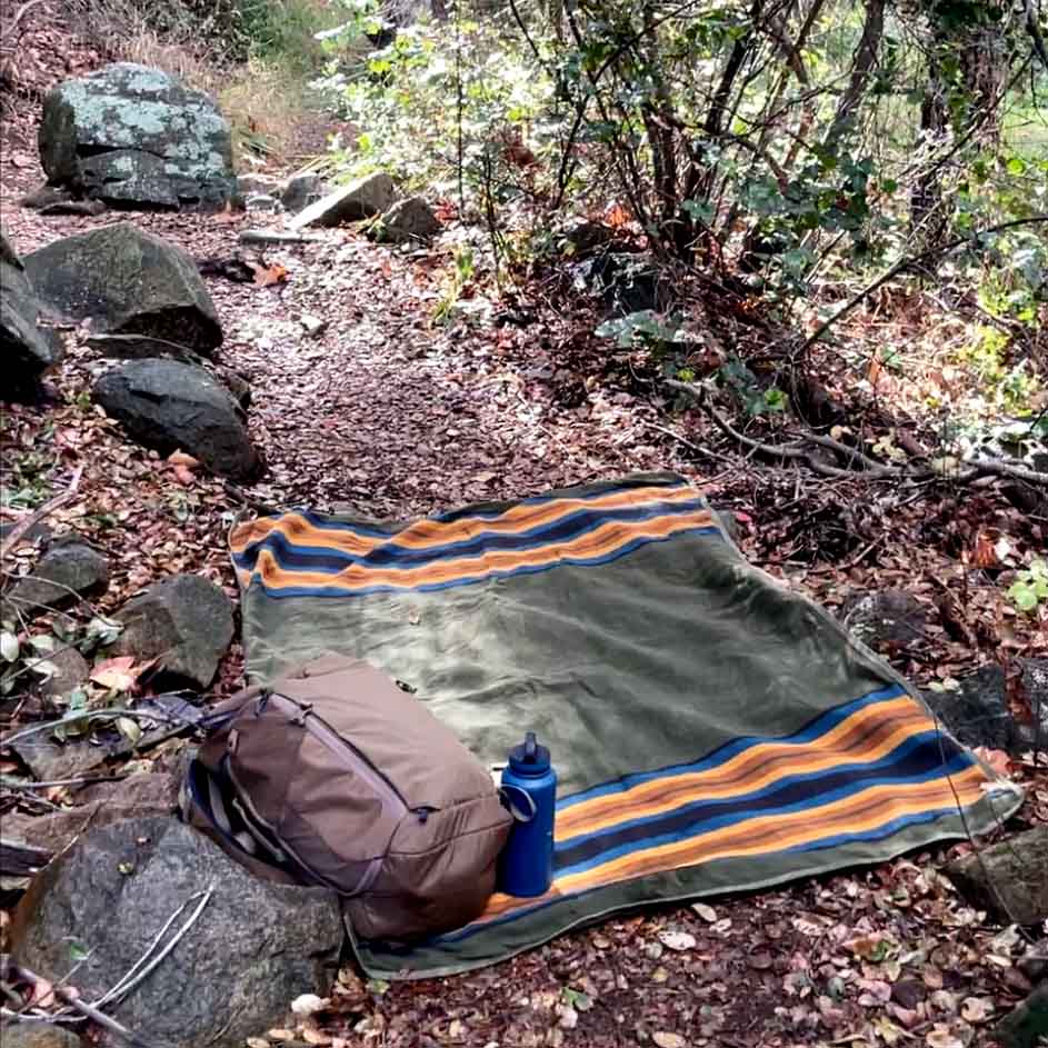 West Path waxed canvas camping blanket spread on outdoor ground, ideal for camping and bushcraft activities.