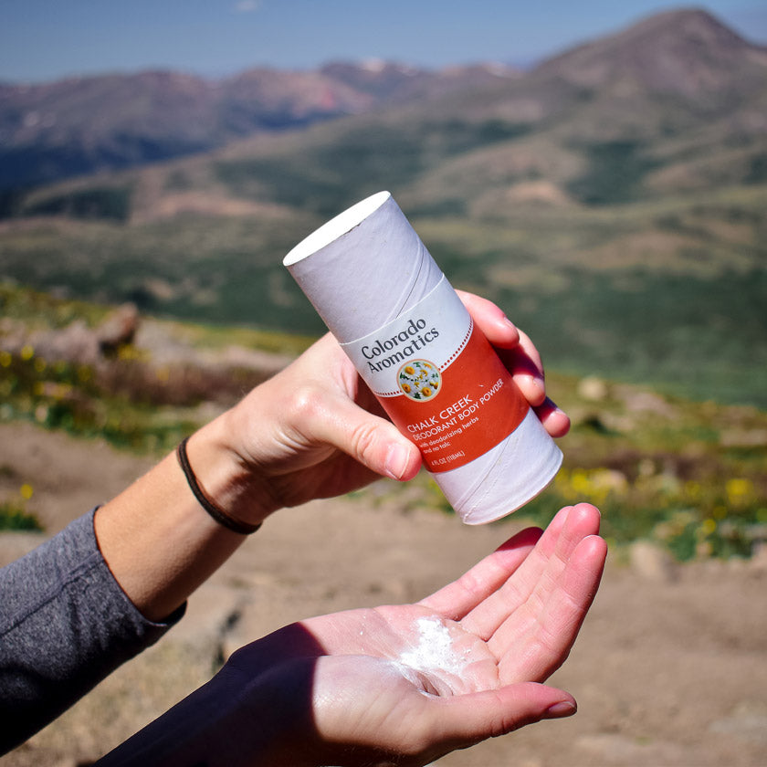 Herbal Chalk Creek Deodorant Powder by Colorado Aromatics displayed on a mountain surface, showcasing natural ingredients and product packaging.