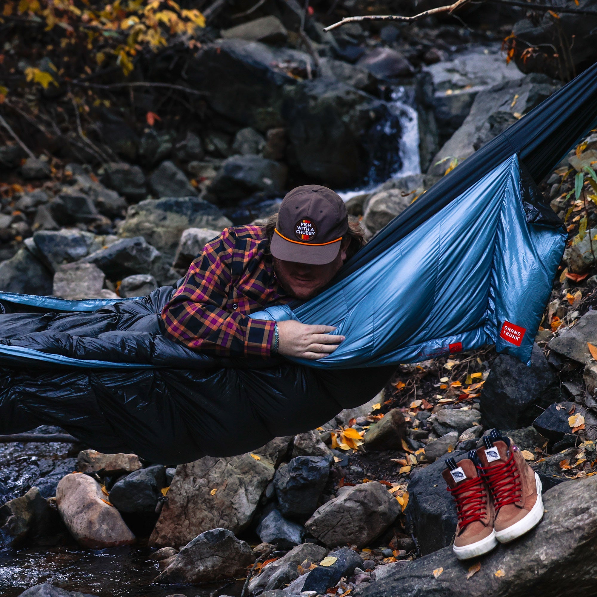 GrandTrunk Evolution 20 Down Sleeping Bag Hammock hanging outdoors with trees and greenery in the background.