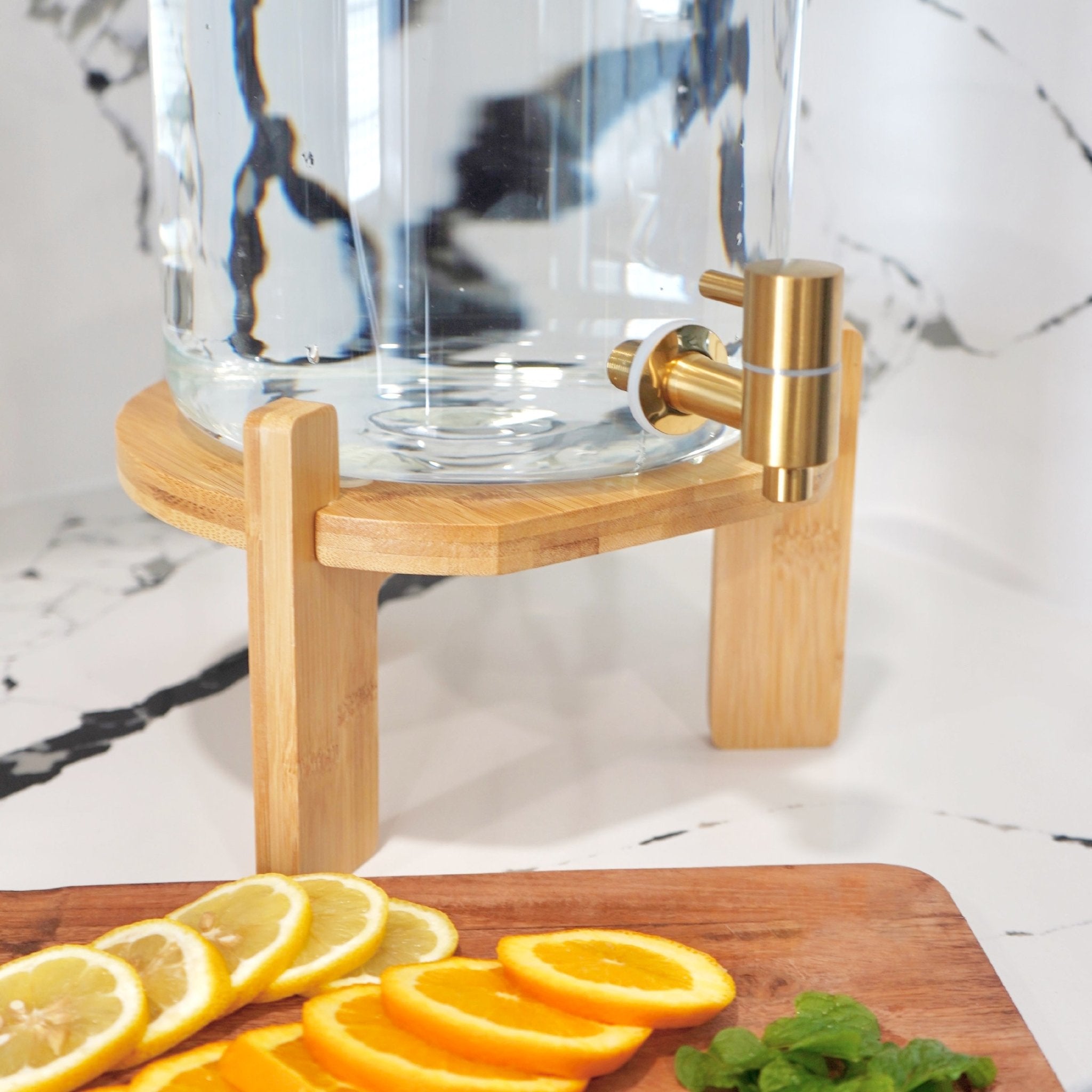 Glass drink dispenser with stand from Tea + Linen, clear glass container suitable for beverages, with a sturdy wooden stand.