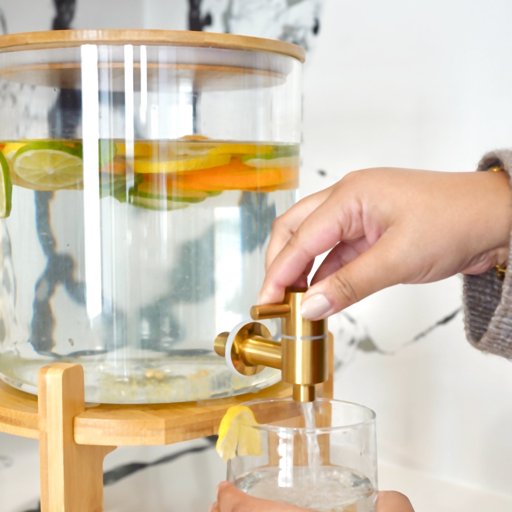 Glass drink dispenser with stand by Tea + Linen, clear glass container for beverages on a sturdy stand, ideal for parties or gatherings.