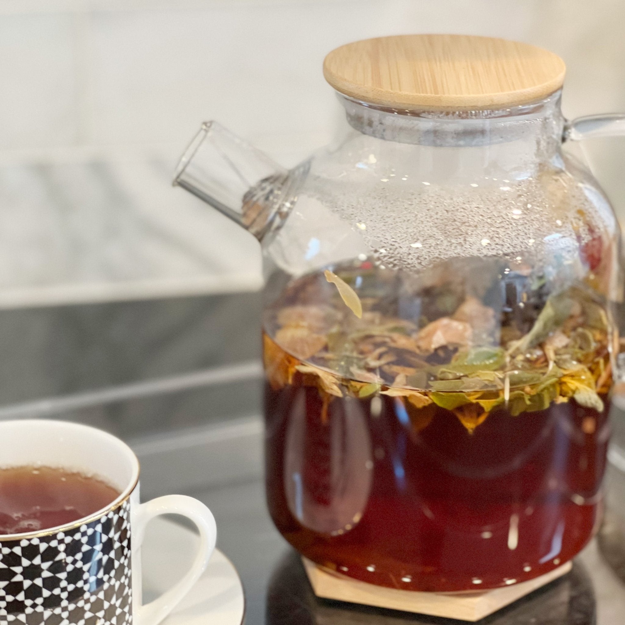 Clear glass teapot with 1800mL capacity from Tea + Linen, featuring a handle, spout, and infuser for brewing tea.