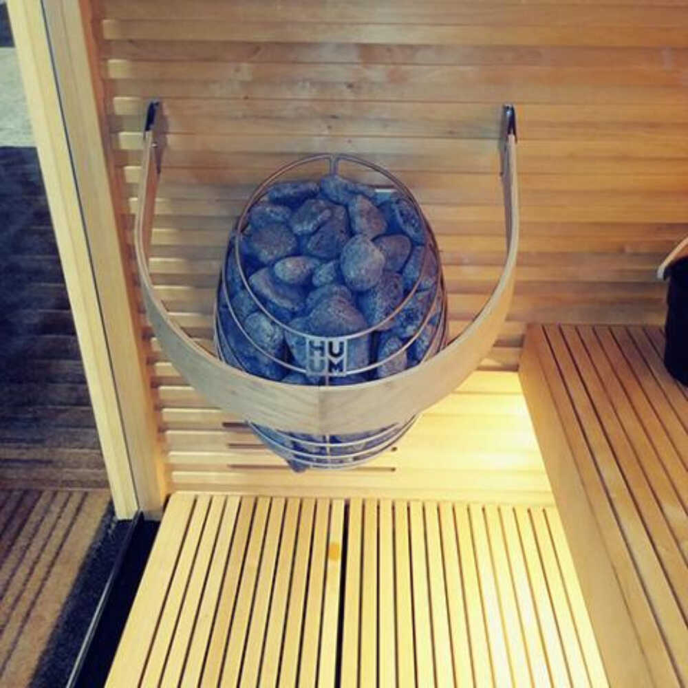 Wall-mounted Huum Drop 240V sauna heater with digital controller and sauna stones, shown inside a sauna room with water-drop design.