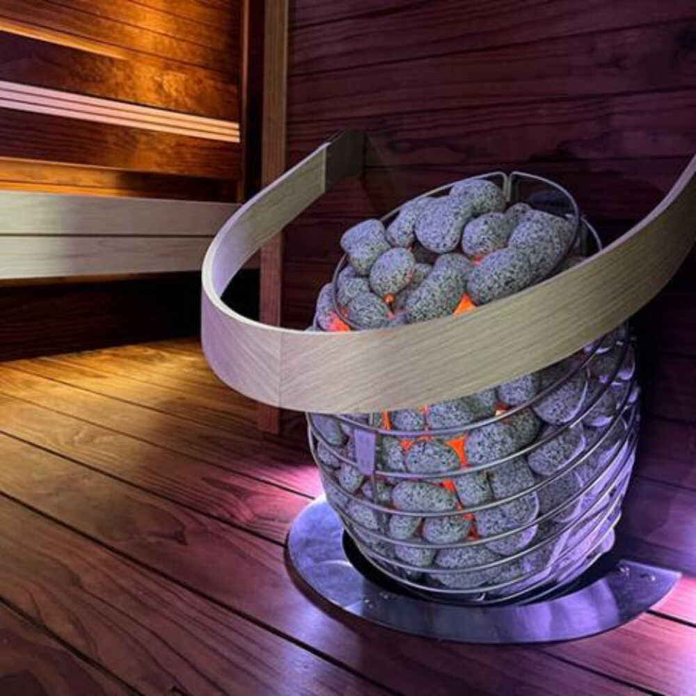 Wall-mounted Huum Drop 240V sauna heater with water-drop design and digital controller, shown from left view with sauna stones.