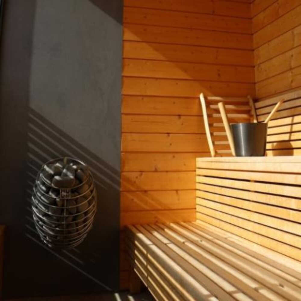 Huum Drop 240V SGS listed wall mount sauna heater with water-drop design, shown in a sauna room with digital controller and stones.
