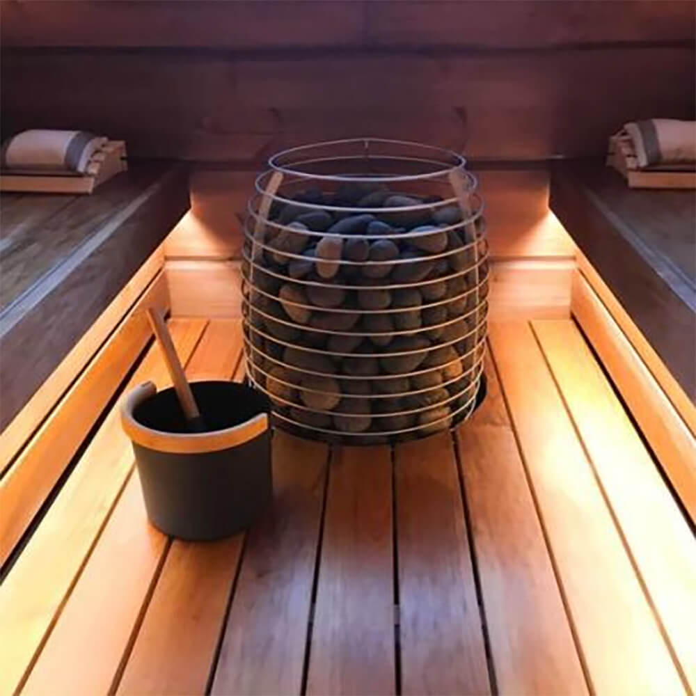 Huum Hive Premium 18kW floor-mounted sauna heater with UKU control and sauna stones inside a modern sauna room with LED lighting.